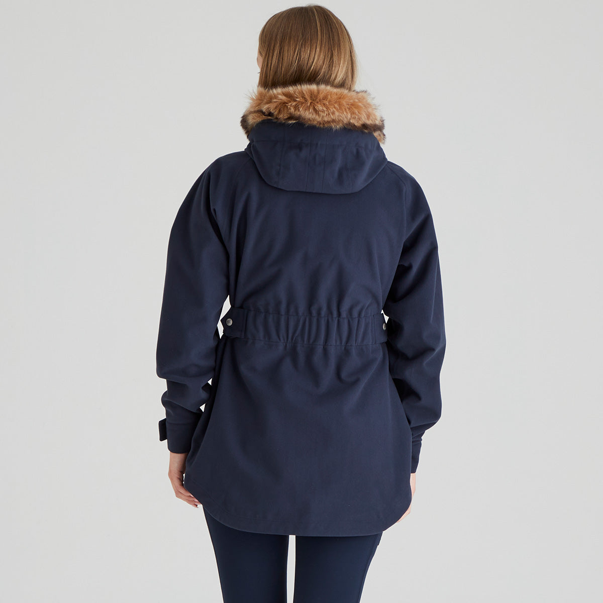 back view of Navy parka waterproof coat with fur hood worn by a person on a light grey background