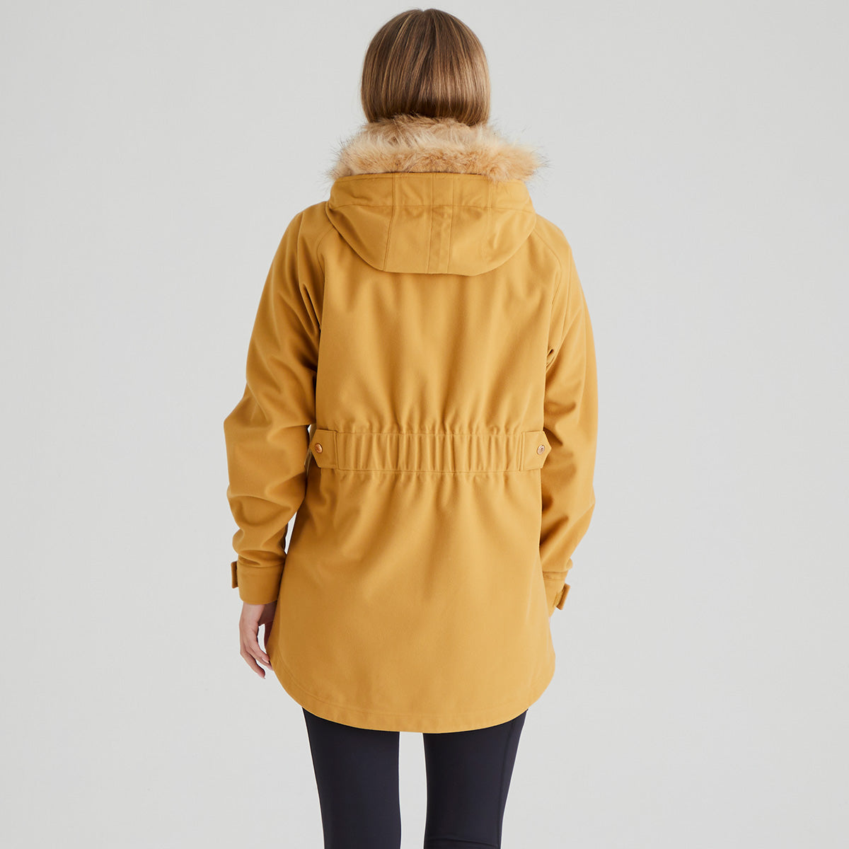 Person wearing a mustard yellow parka with fur hood on a light grey background