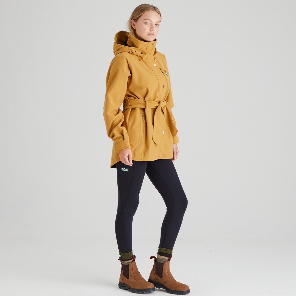 Woman wearing a mustard yellow jacket on a light grey background