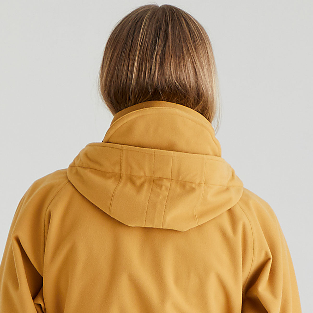 Person wearing a mustard yellow raincoat on a plain background