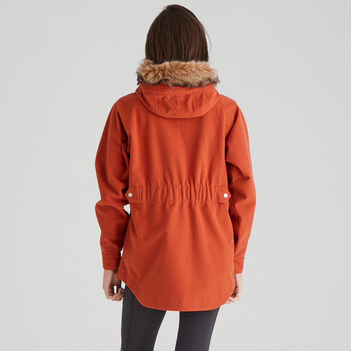 Person wearing an orange coat with a fur-lined hood on a gray background