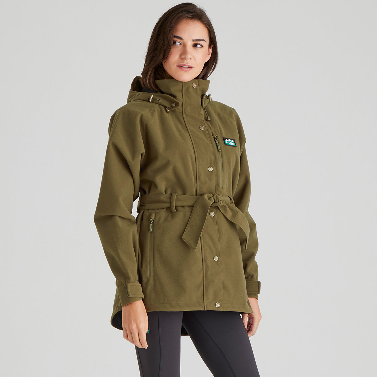Woman wearing a green jacket with a brand logo on a grey background