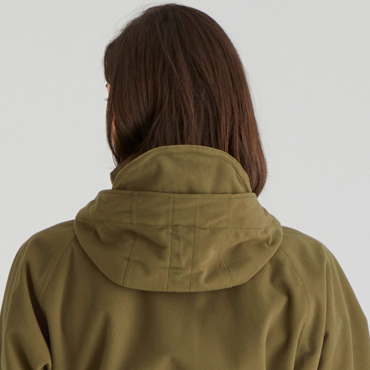 Back of person wearing a green jacket with a plain background