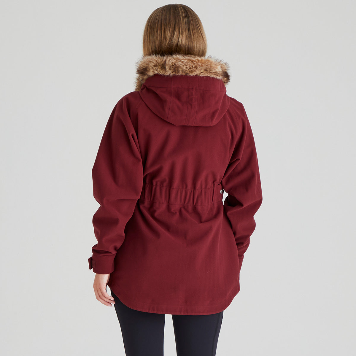 Red parka with fur hood worn by a person on a light grey background