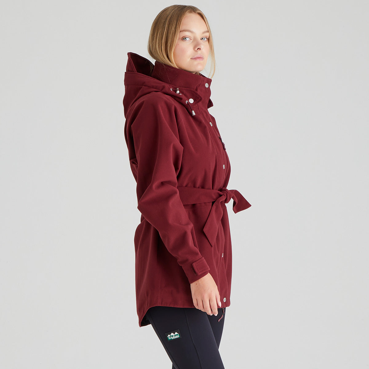 Woman wearing a burgundy hooded coat on a grey background