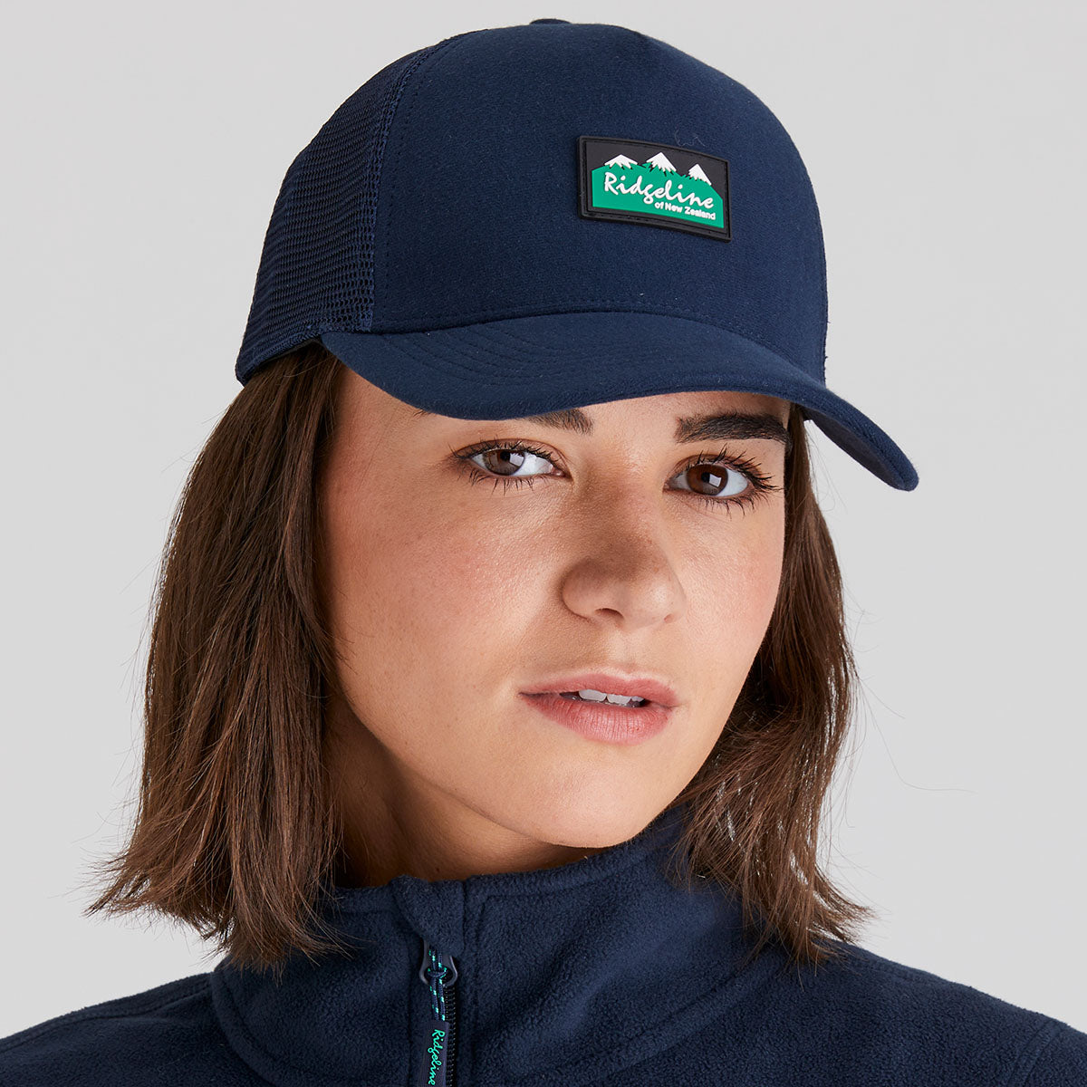 woman wearing a navy blue cap with a ridgeline clothing logo on a grey background