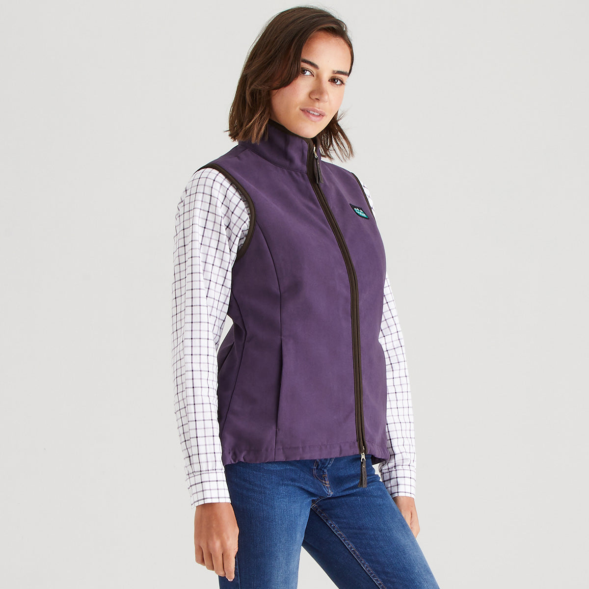 Woman wearing a purple vest over a checkered shirt with a gray background