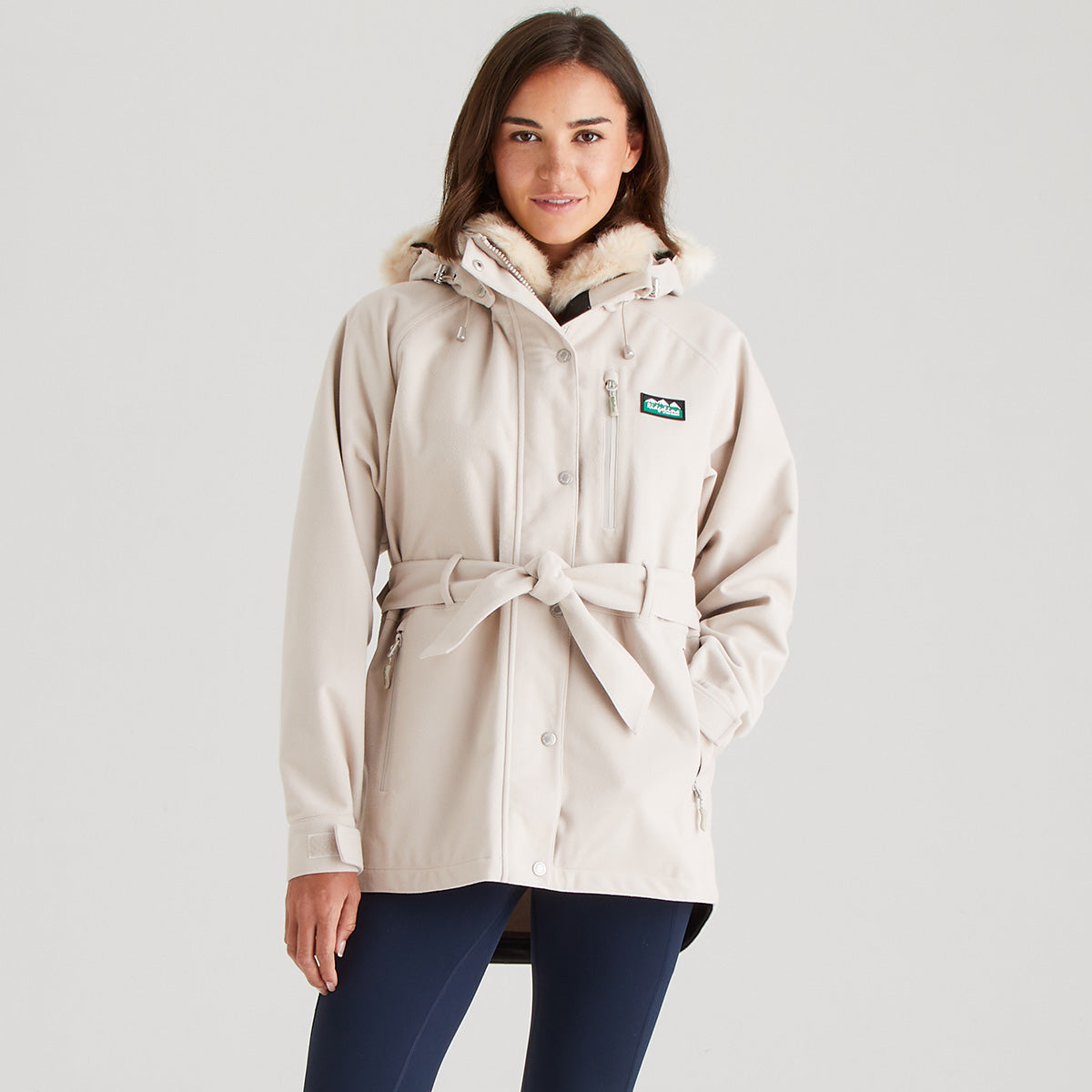 Woman wearing a cream parka with a visible brand logo on a light gray background