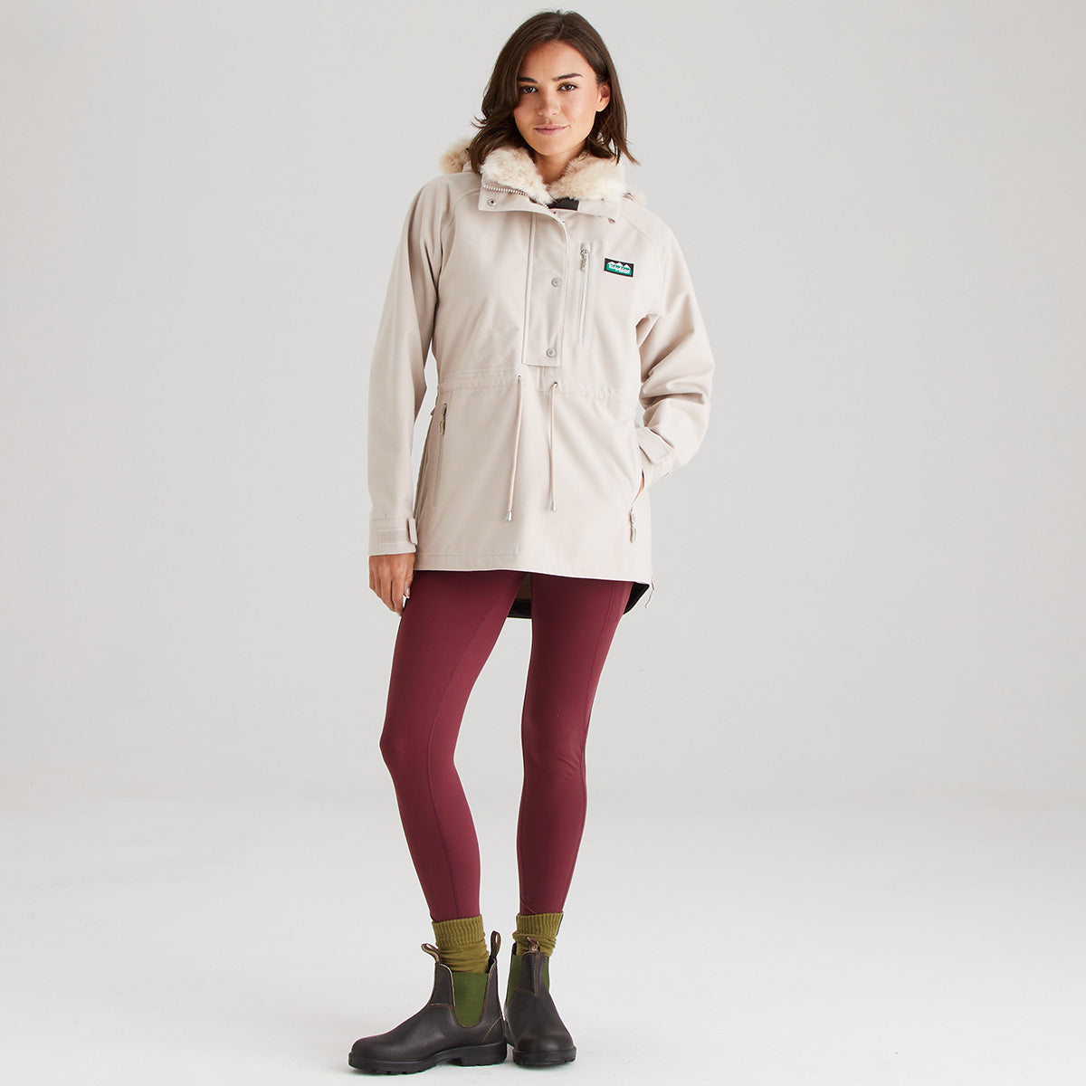 Woman wearing a cream jacket with a brand logo on a white background