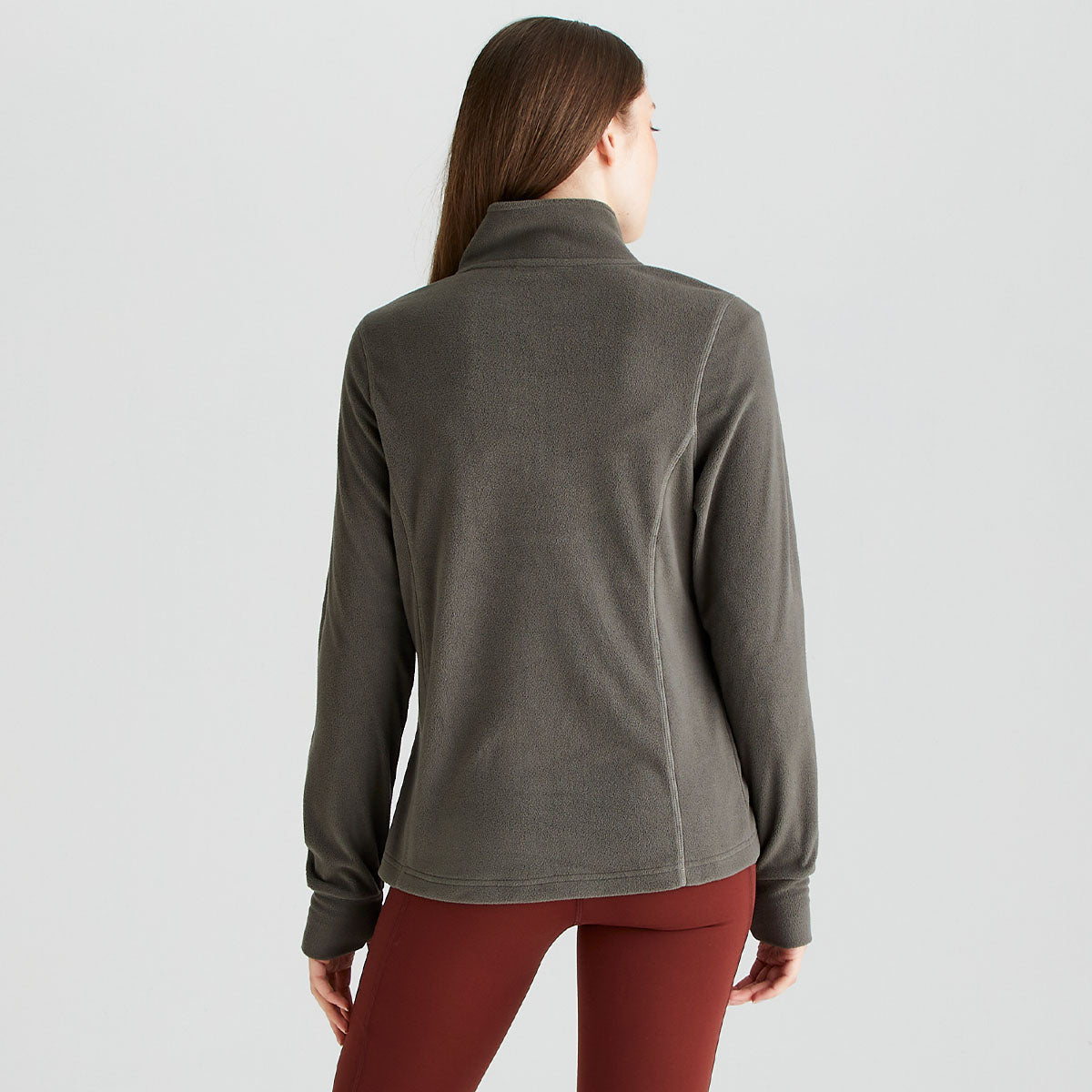 Rear view of a grey Ridgeline quarter-zip fleece pullover worn with rust-red performance leggings. The pullover features a high stand-up collar, long sleeves, and a soft fleece construction for warmth and comfort. Shaped side seams create a streamlined, feminine fit, while the clean back design showcases the pullover’s simple outdoor styling. Photographed against a plain light-grey studio background, the image highlights the fit and coverage of the Ridgeline fleece from the rear.