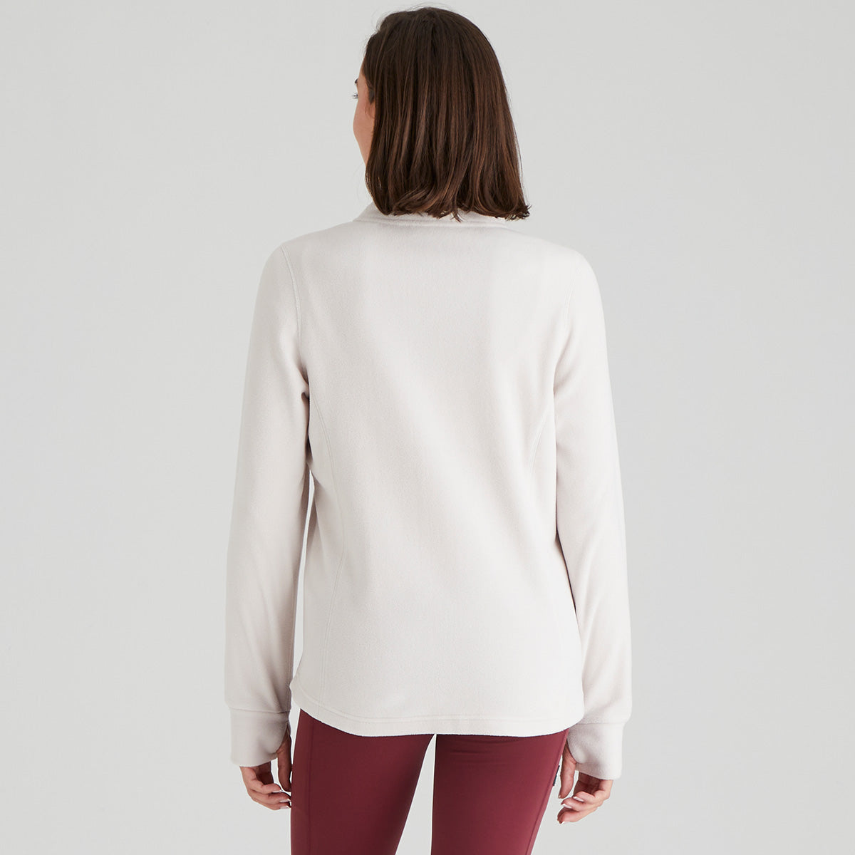 Person wearing a white/ light cream fleece and maroon pants on a light grey background