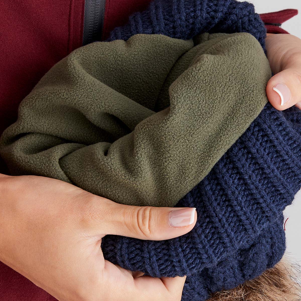 Close-up of hands holding a stack of folded clothes in green and navy.