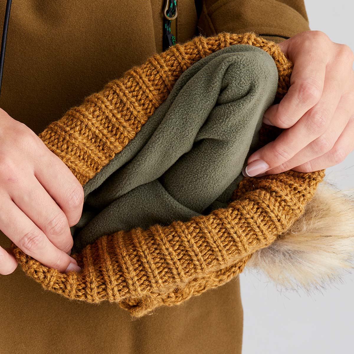 Person holding a knitted brown beanie hat with a fur-lined interior