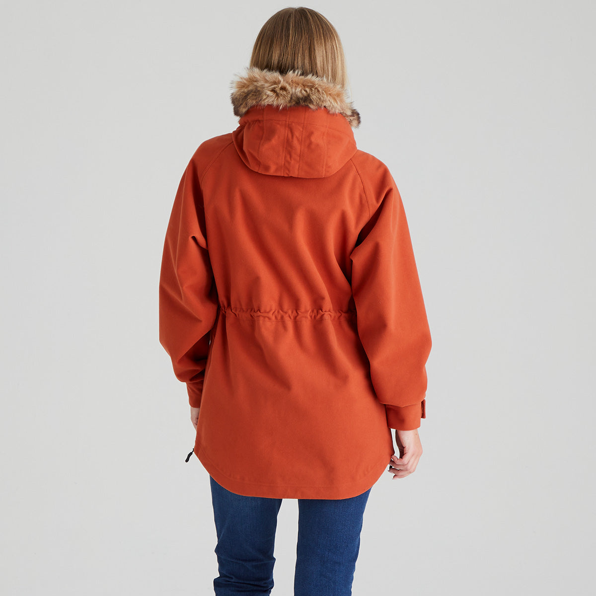 Person wearing an orange coat with fur-lined hood on a plain background