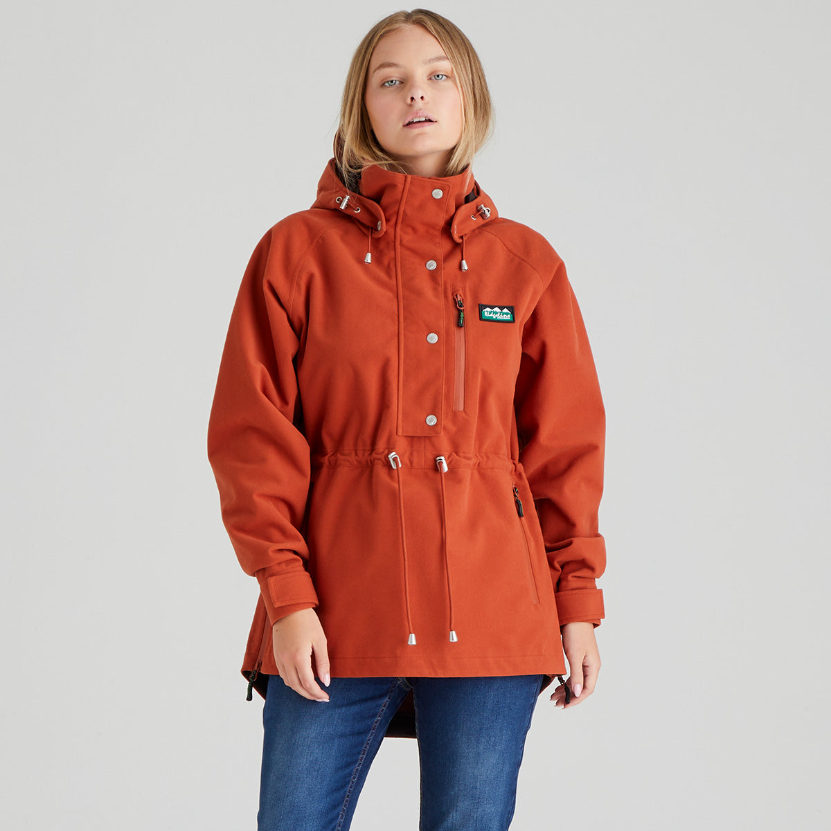 Person wearing an orange jacket with a brand logo on a grey background