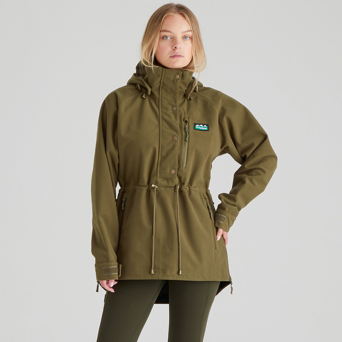 Woman wearing a green jacket with a brand logo on a grey background