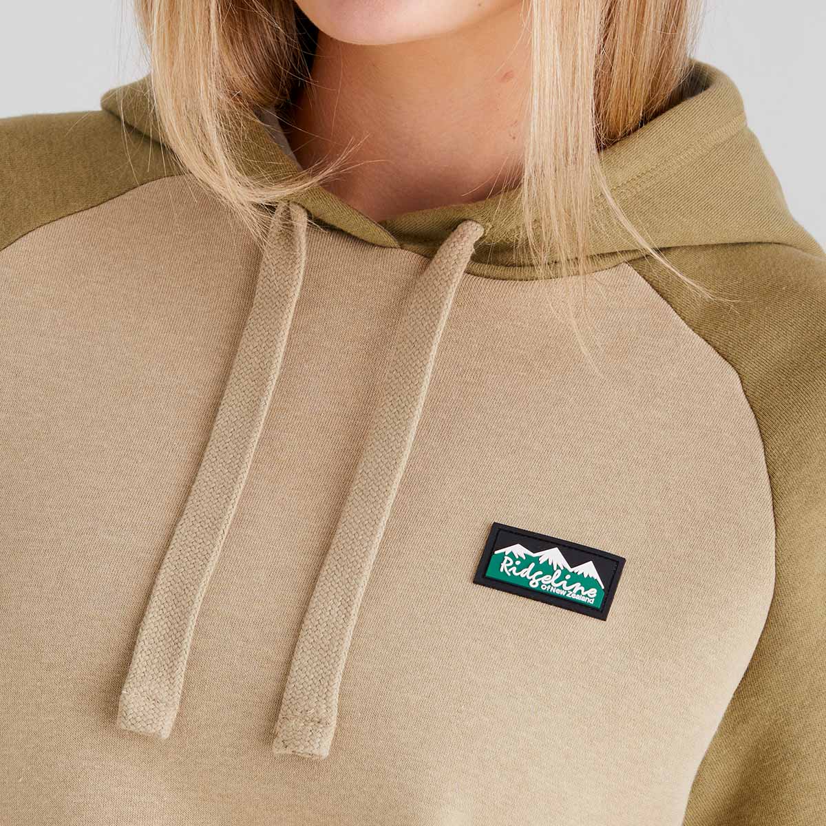 Beige and brown hoodie with a visible brand logo on a plain background