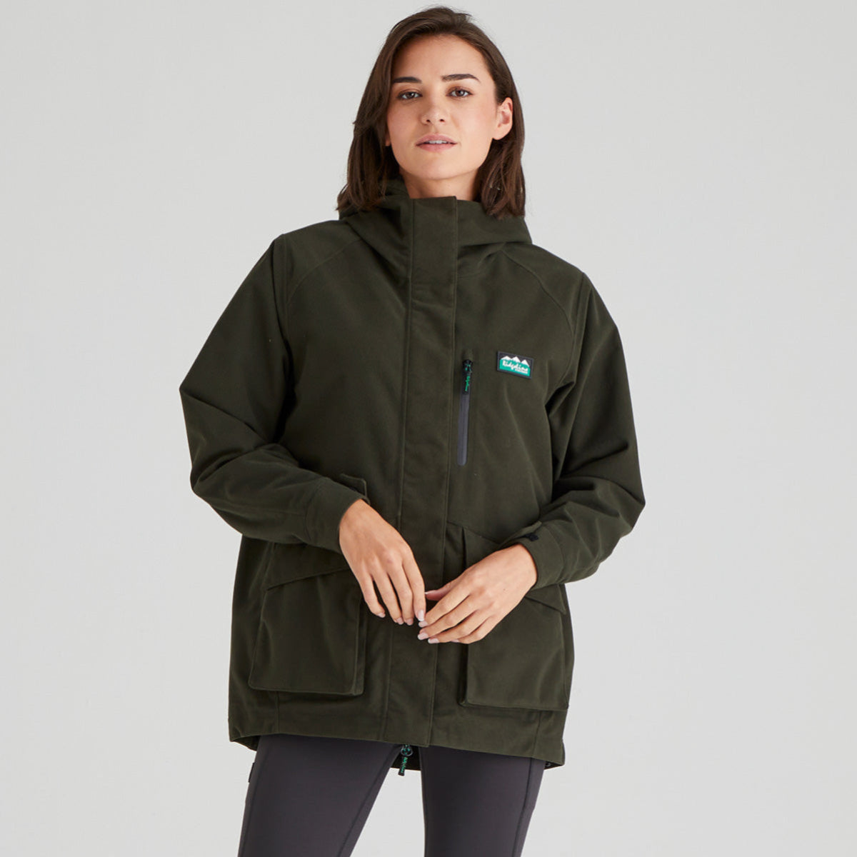 Woman wearing a green jacket with a brand logo on a grey background