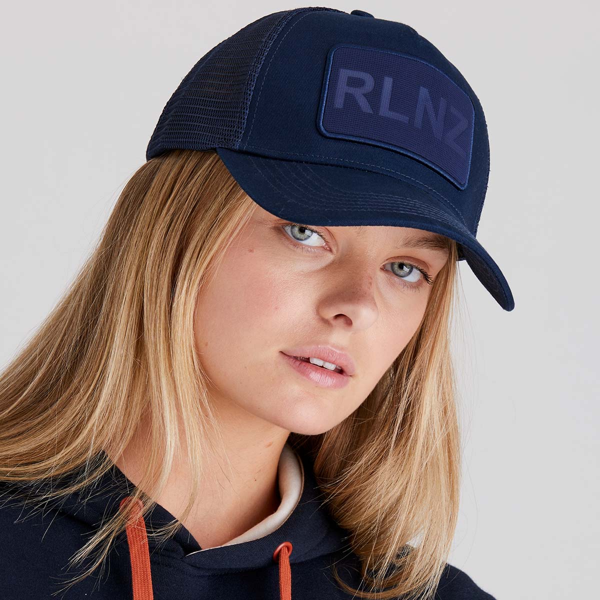 woman wearing a navy blue cap with 'RLNZ' logo on a light grey background