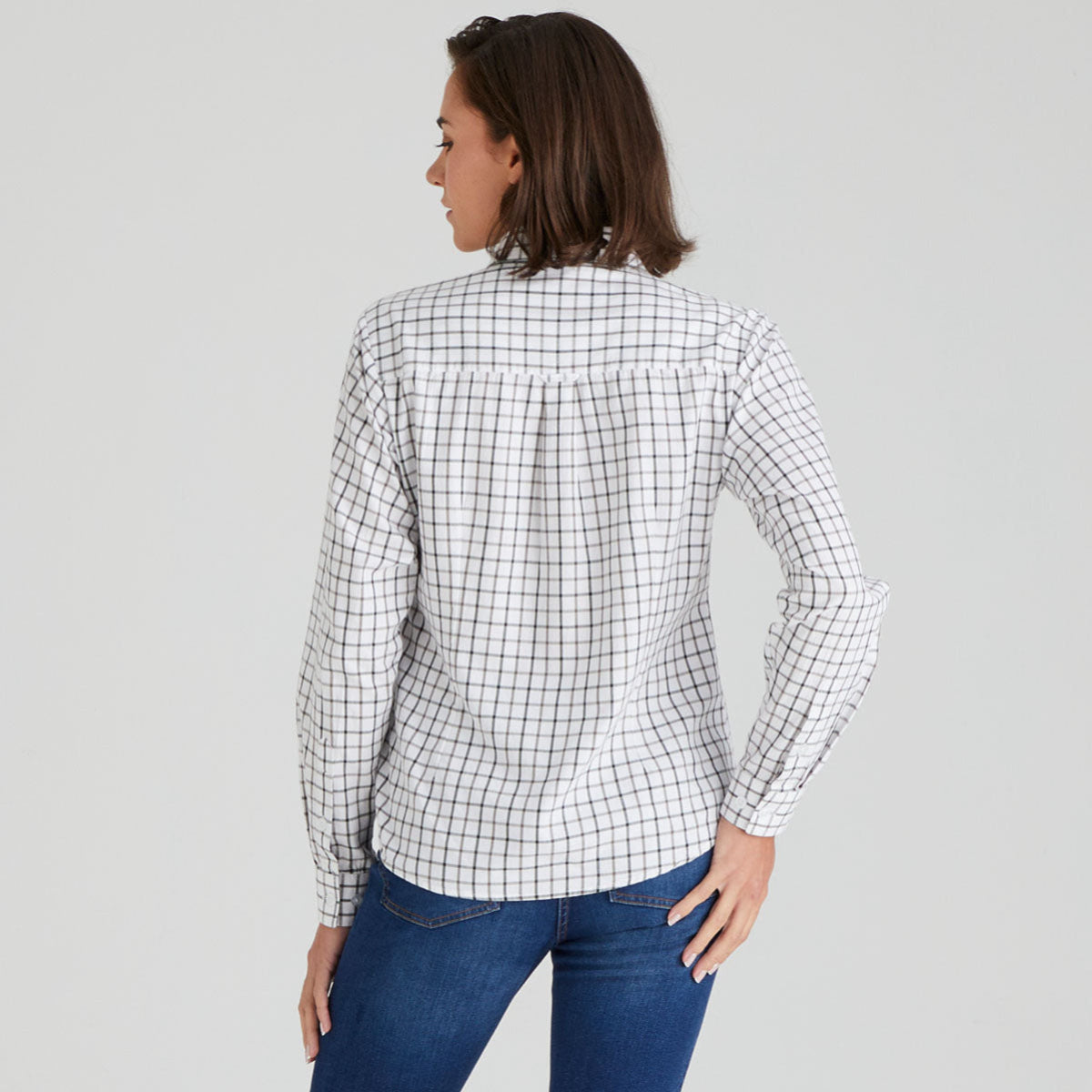 Woman wearing a white shirt with black grid pattern and blue jeans on a grey background