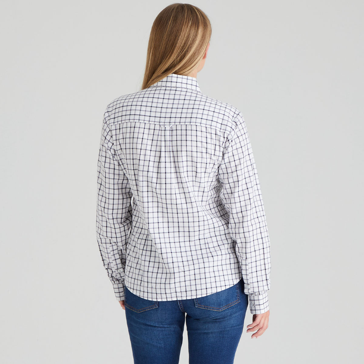 Back of person wearing a white shirt with black grid pattern and blue jeans on a grey background