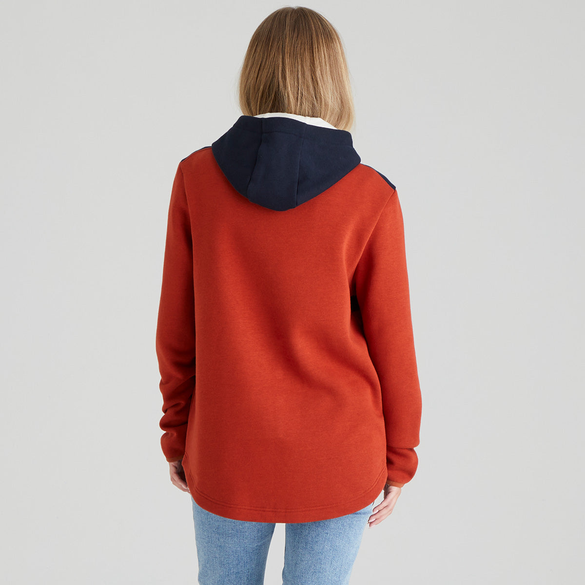 back view of person wearing a orange hoodie with navy hood on a plain background
