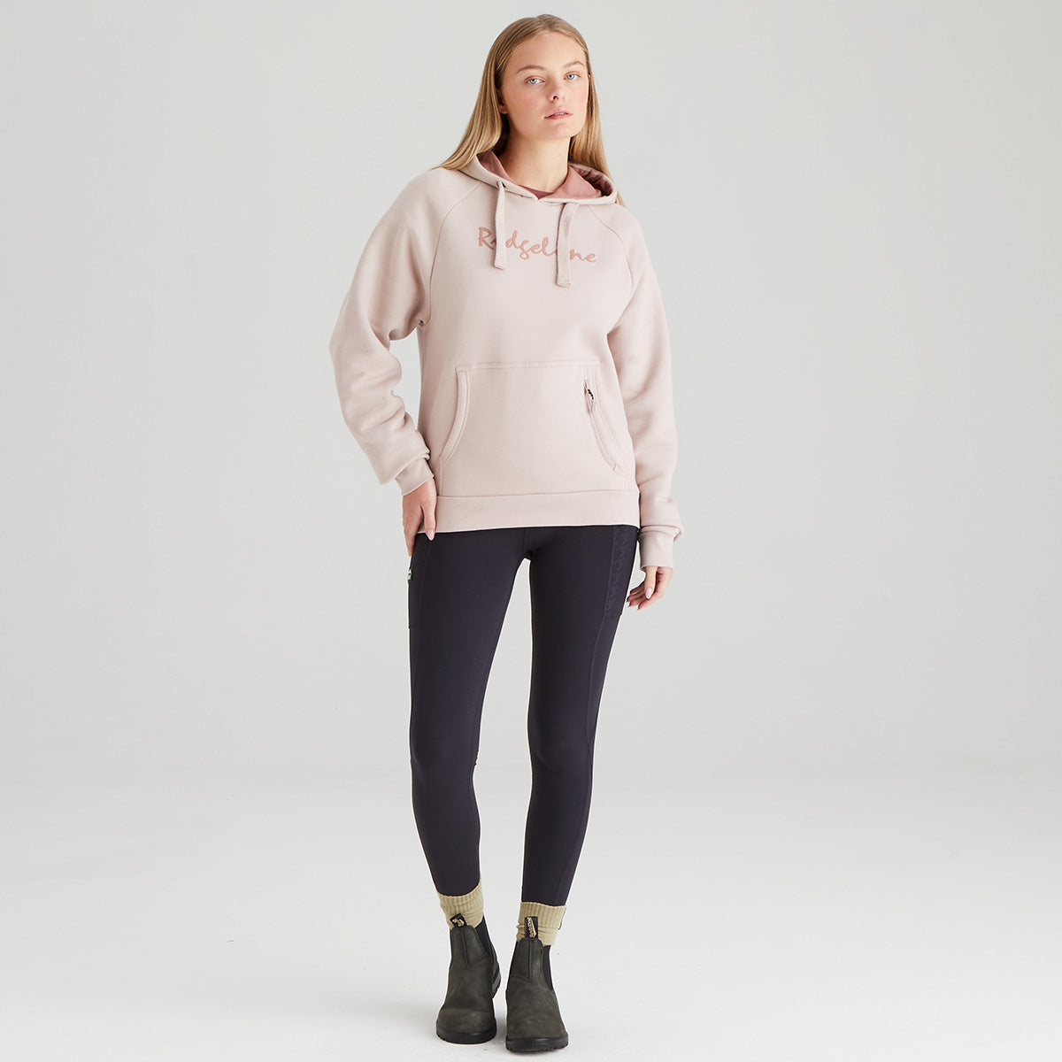 Woman wearing a light pink hoodie with text and dark leggings on a white background