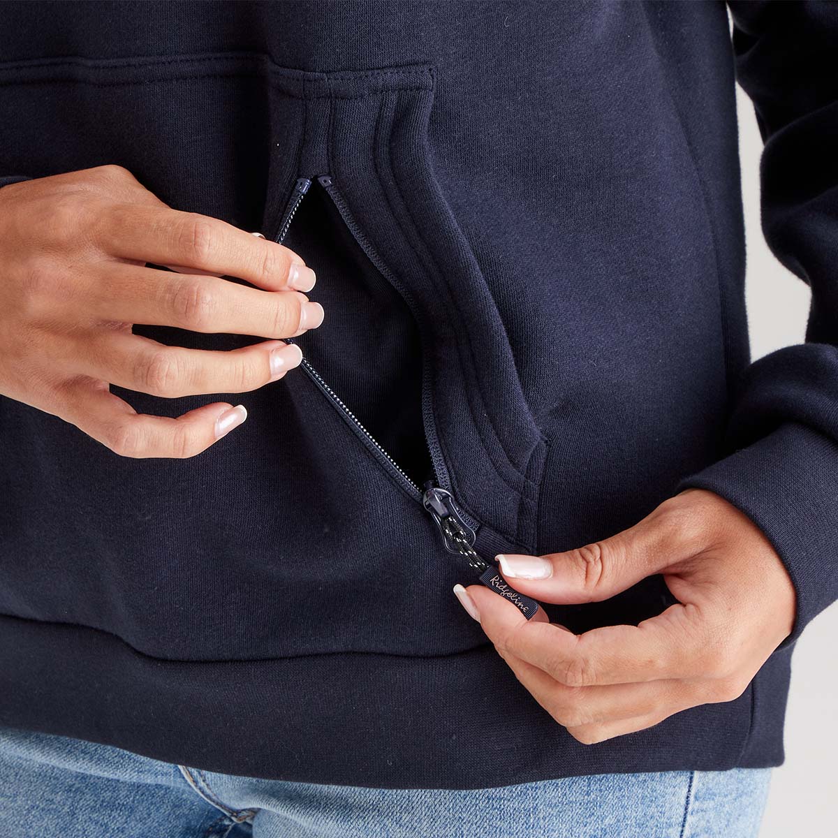 Person zipping up a navy blue hoodie with light blue jeans.