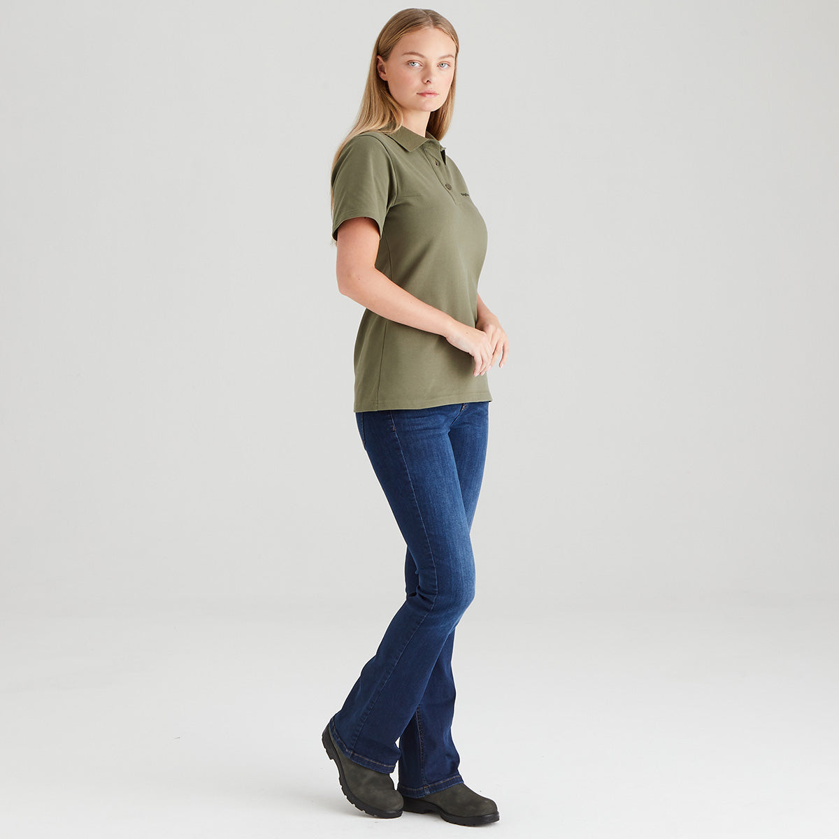 Woman wearing an olive green polo shirt and blue jeans on a white background