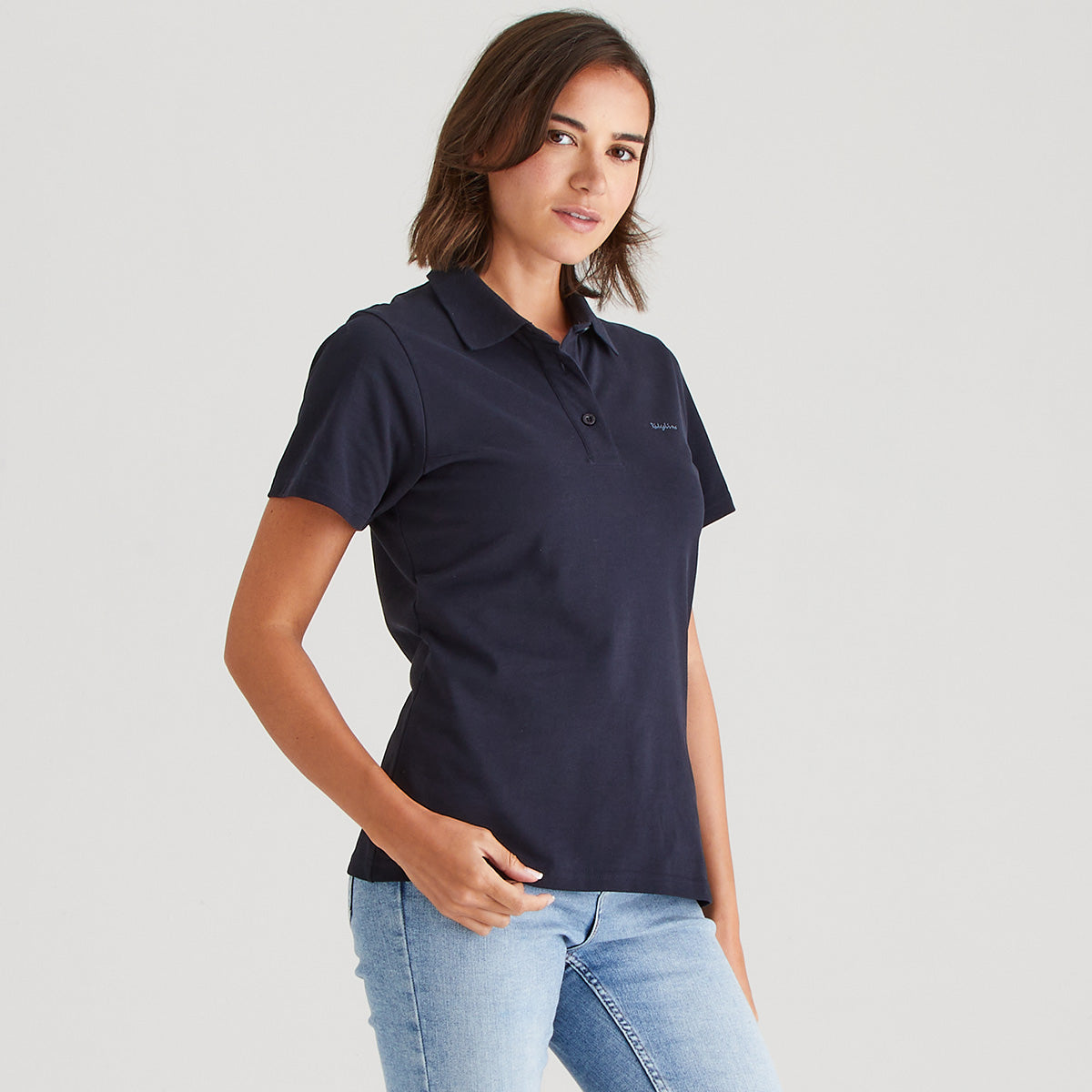 Woman wearing a navy polo shirt and light blue jeans on a gray background