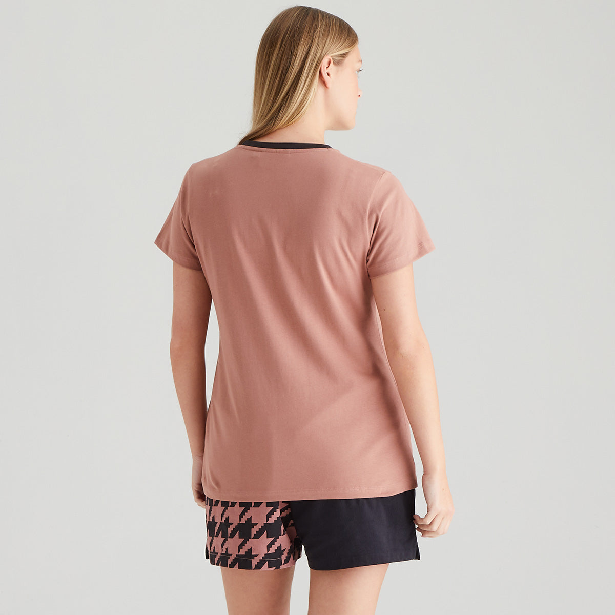 Woman wearing a pink t-shirt and patterned shorts on a gray background