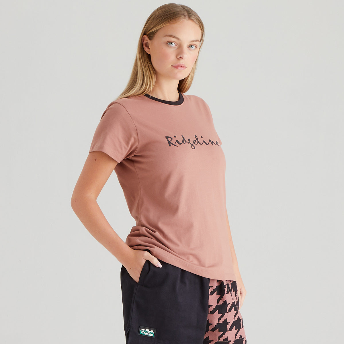 Woman wearing a pink t-shirt with 'Ridgeline' branding on a light gray background