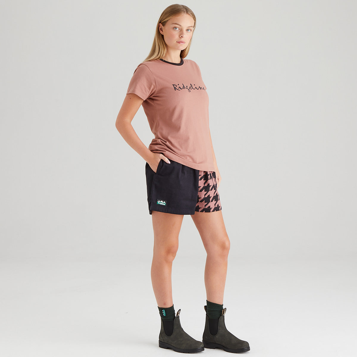 Woman wearing a pink t-shirt and black shorts with a patterned bottom on a white background