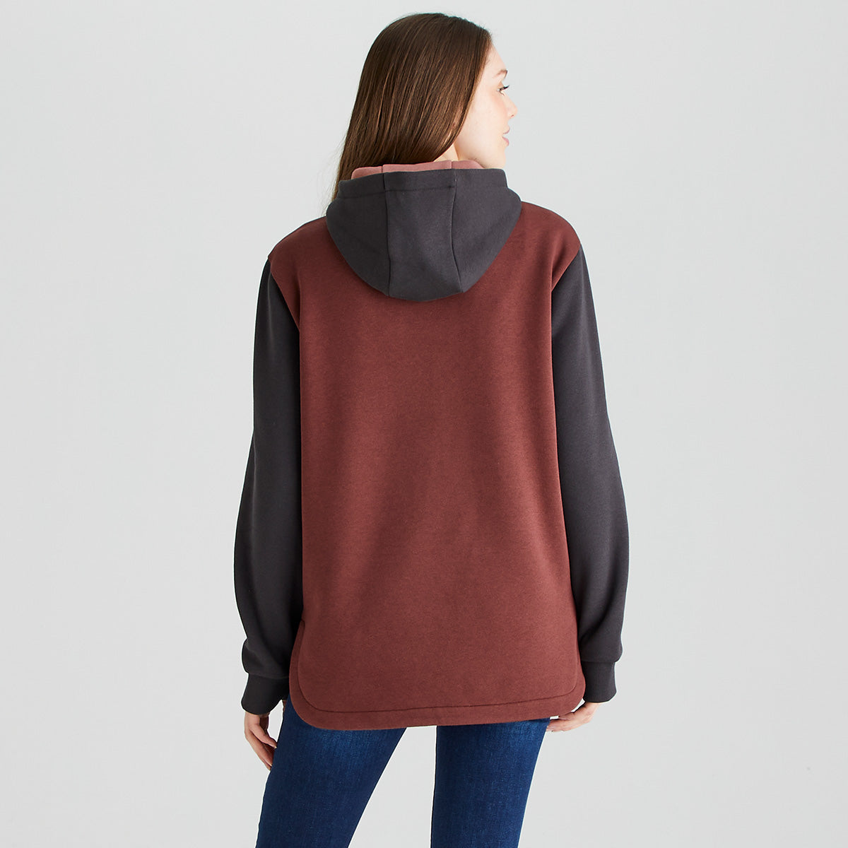 Rear view of a person wearing a Ridgeline heavyweight hoodie in brown and black with a contrasting hood, shown with blue jeans against a light grey studio background.