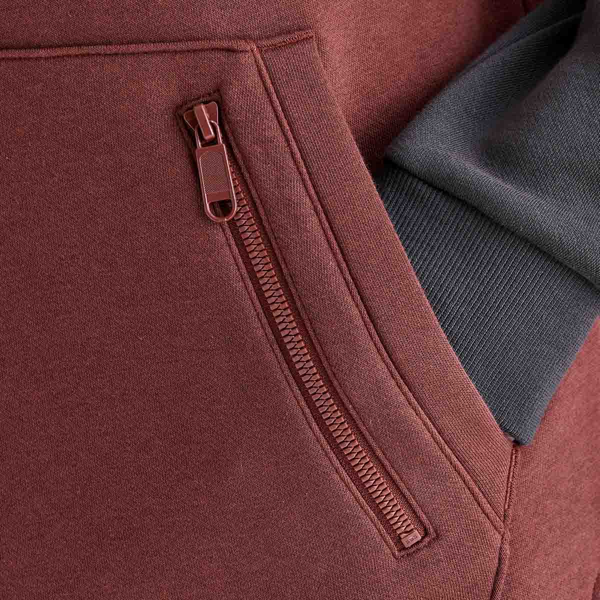 Close-up detail of a Ridgeline heavyweight hoodie showing the zipped security pocket integrated into the kangaroo pocket, with brown fabric and contrasting black ribbed cuff.