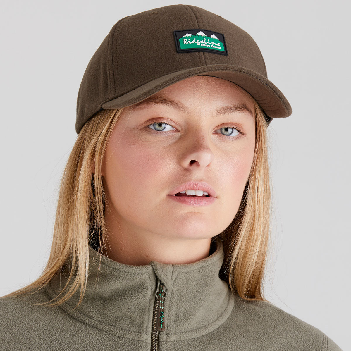woman wearing a brown cap with a logo and a matching jacket on a light grey background