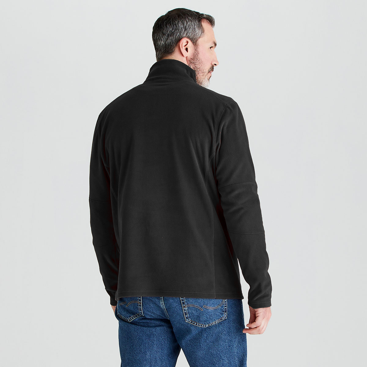 A man viewed from the back wearing a black long-sleeve quarter-zip fleece jacket and blue jeans, set against a plain light gray studio background.