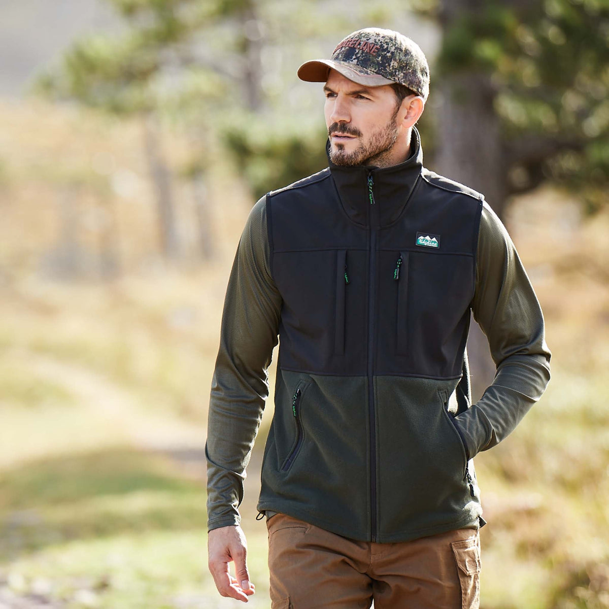 man wearing Two-tone black and green Windproof fleece gilet with a Ridgeline Clothing logo walking through trees
