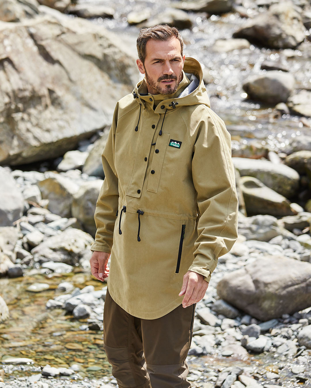 Man wearing a beige jacket standing by a rocky stream