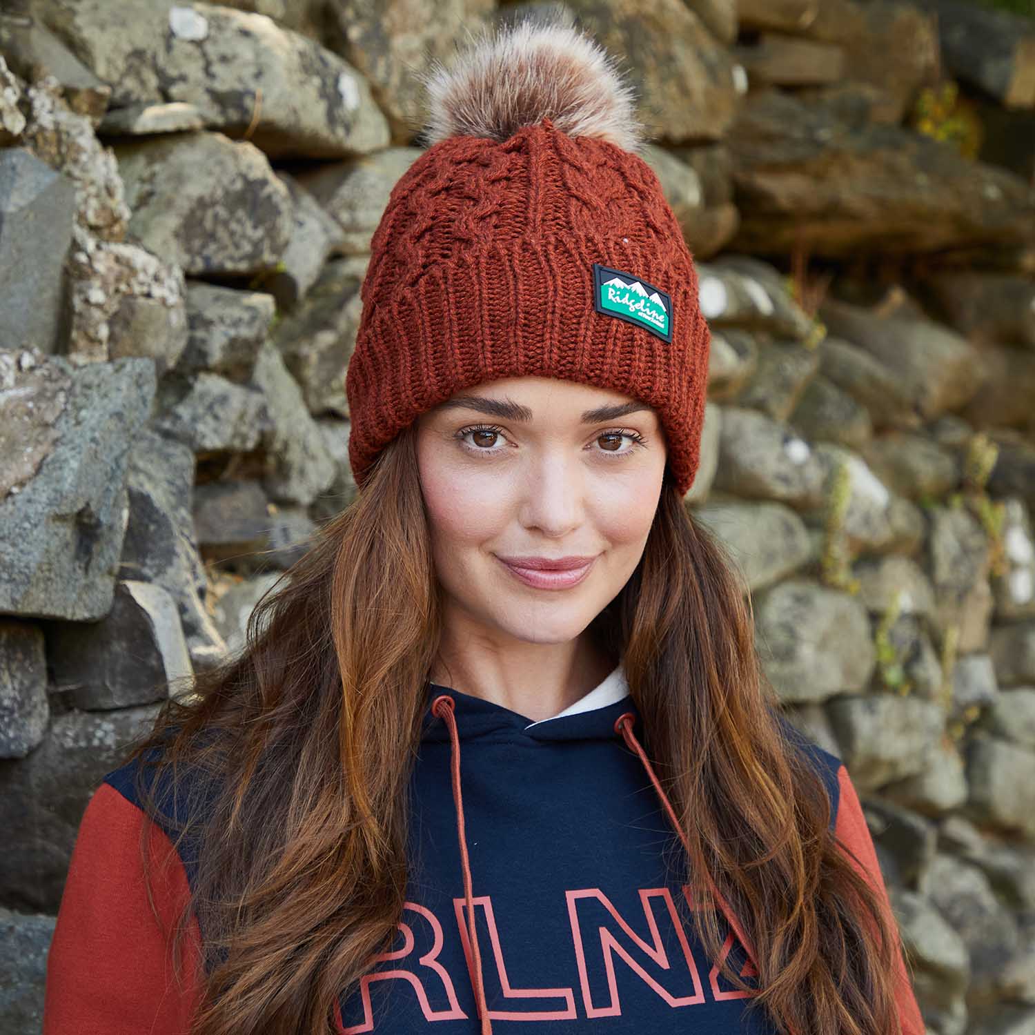 Women in warm bobble hat against a stone wall.