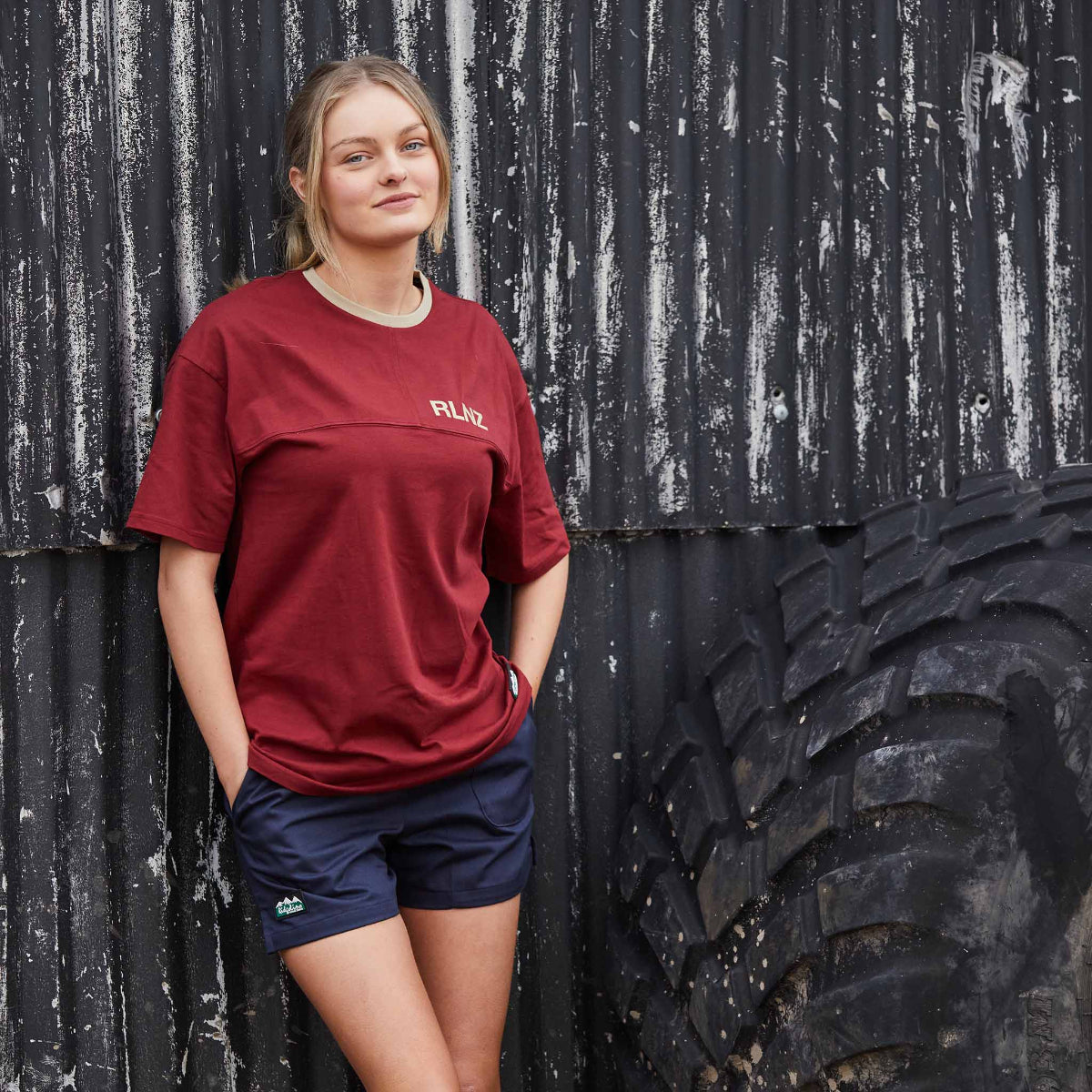 Woman wearing a Red t-shirt with 'RLNZ' logo next to a tractors tire