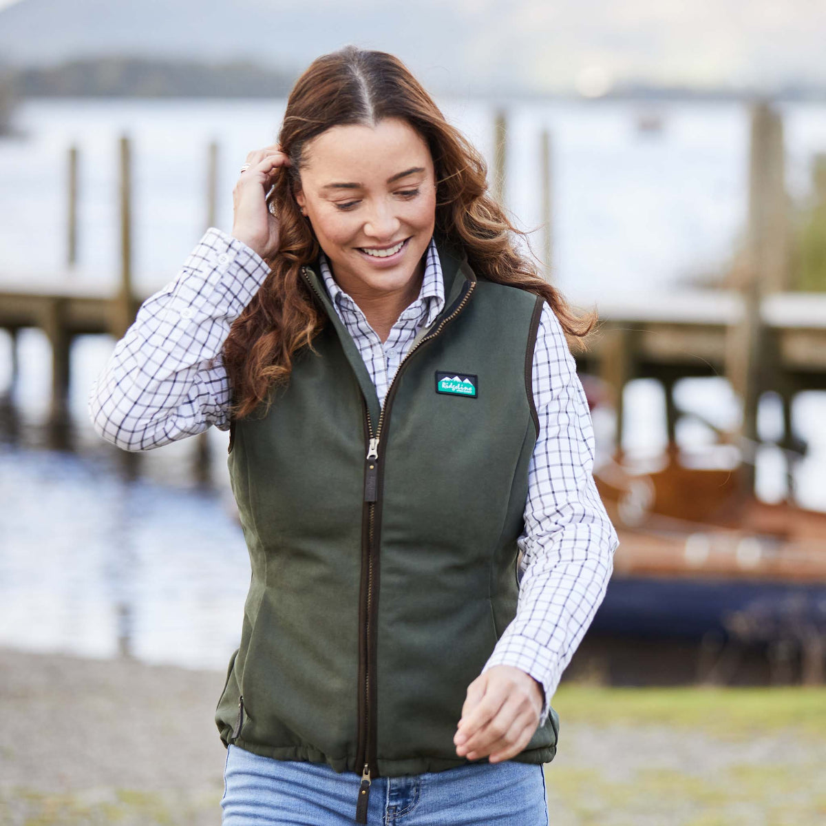 Woman wearing a green Gilet vest with a blurred background of water and boats