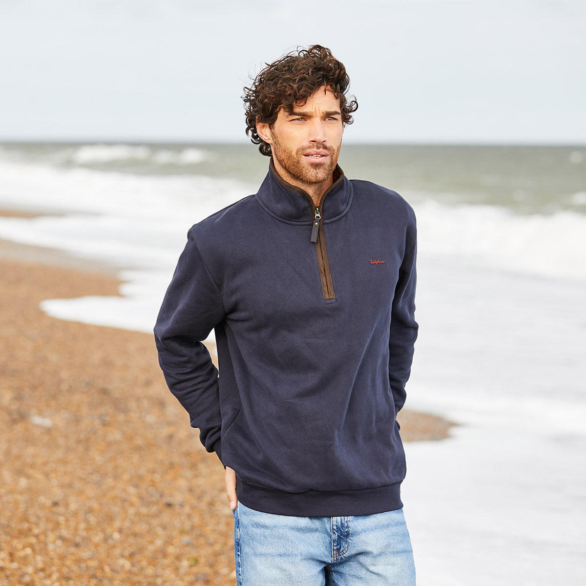 Man wearing a navy blue pullover walking along coast 