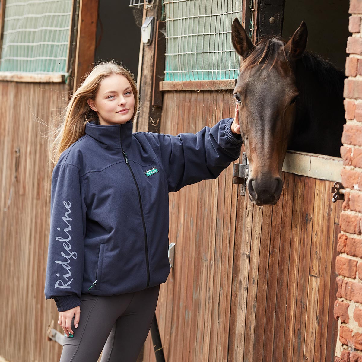 Woman in a navy blue jacket with a horse in a stable