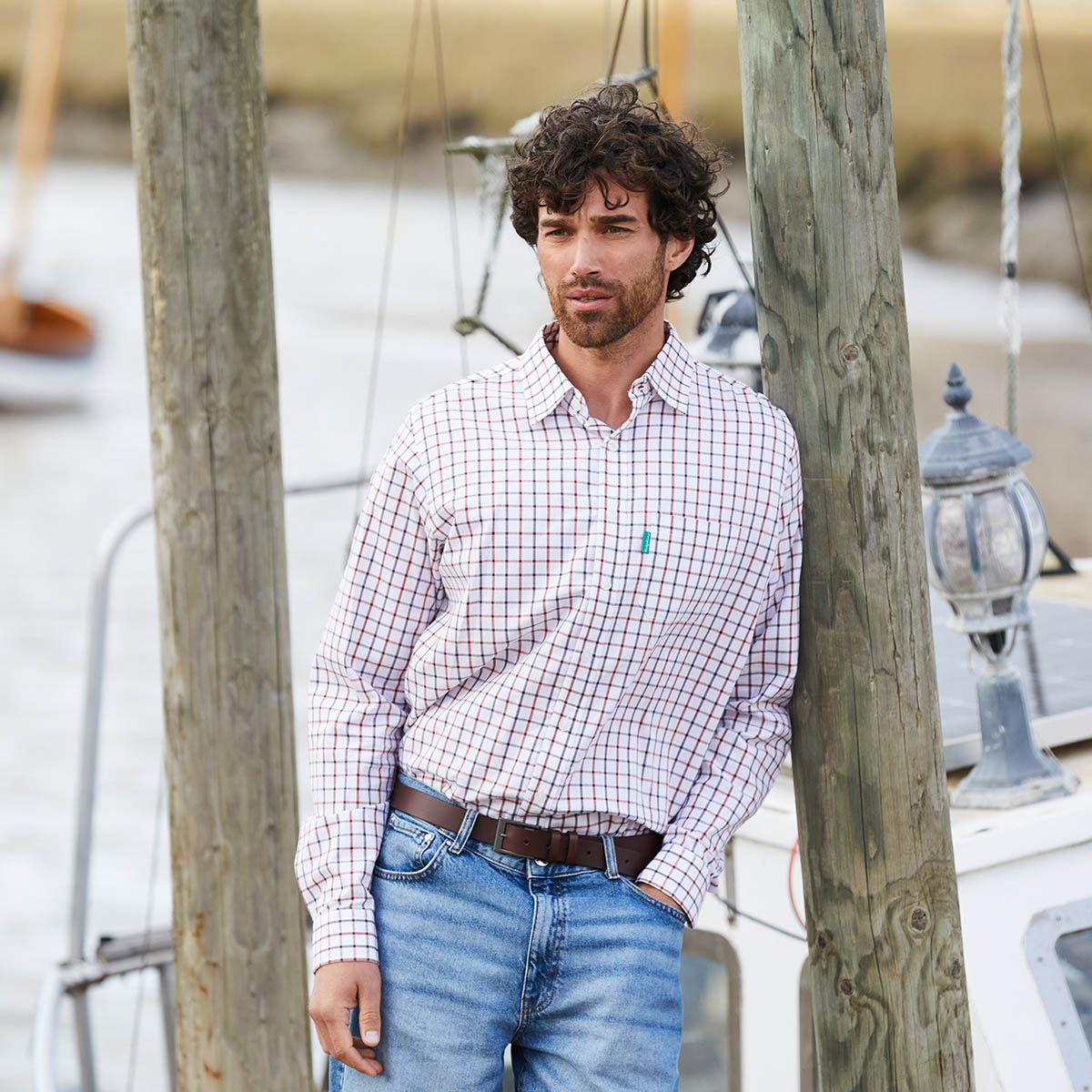 Man wearing a checkered shirt leaning on wooden pole
