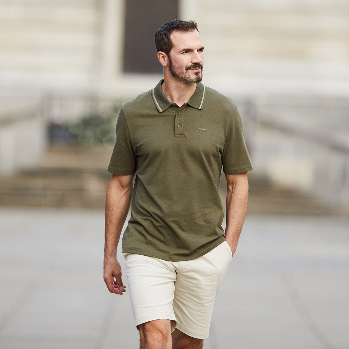 Man wearing white Chino Shorts with green polo with blurred background