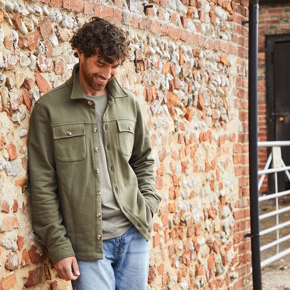 Man wearing a green jacket leaning on a brick wall