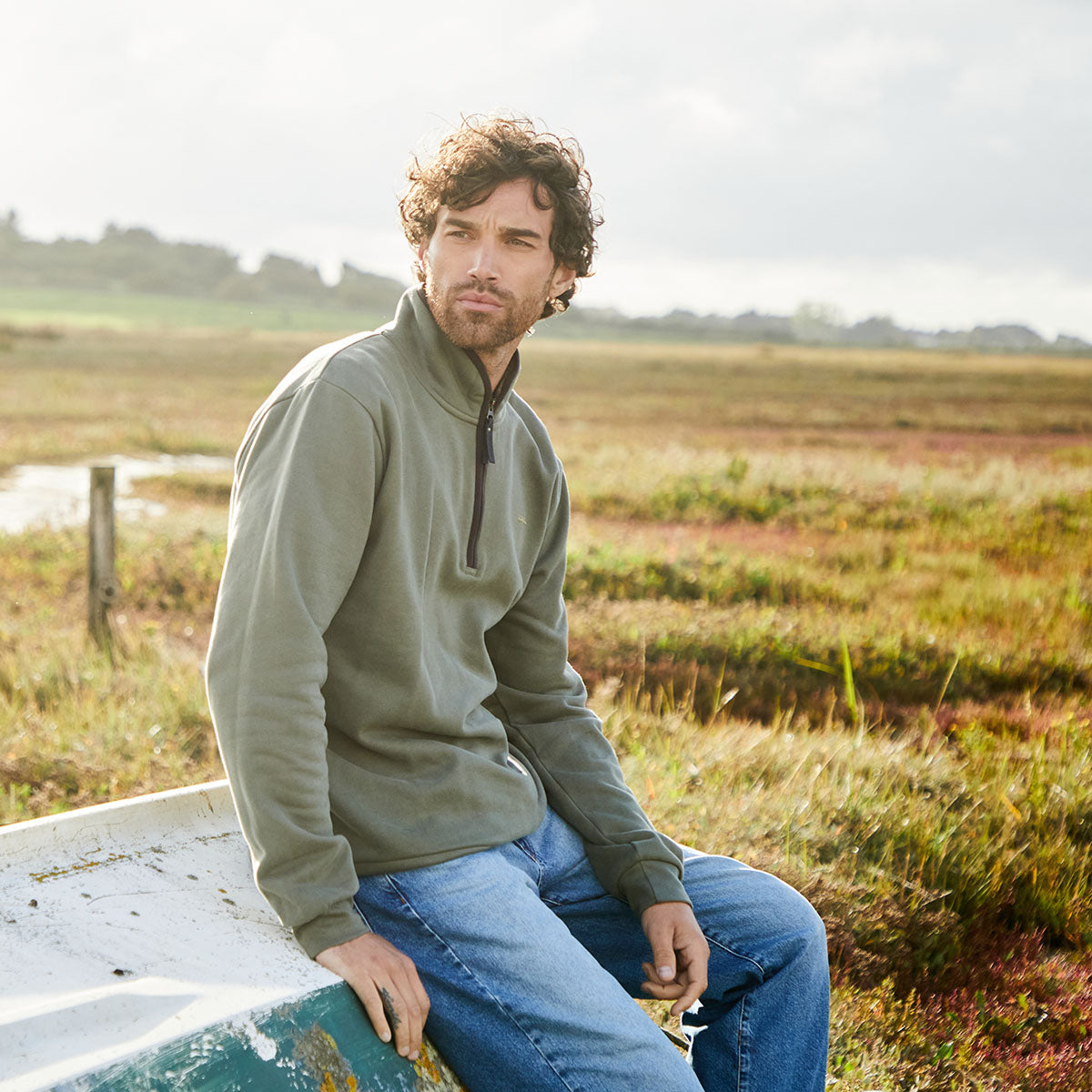 Man wearing a green pullover sitting in field of grass