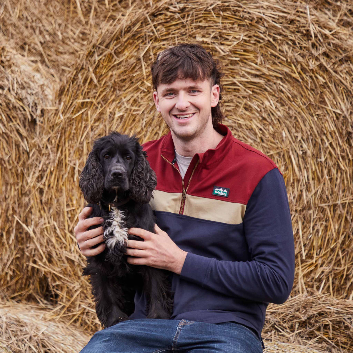 Man holding a black dog in front of hay bales in a Ridgeline top