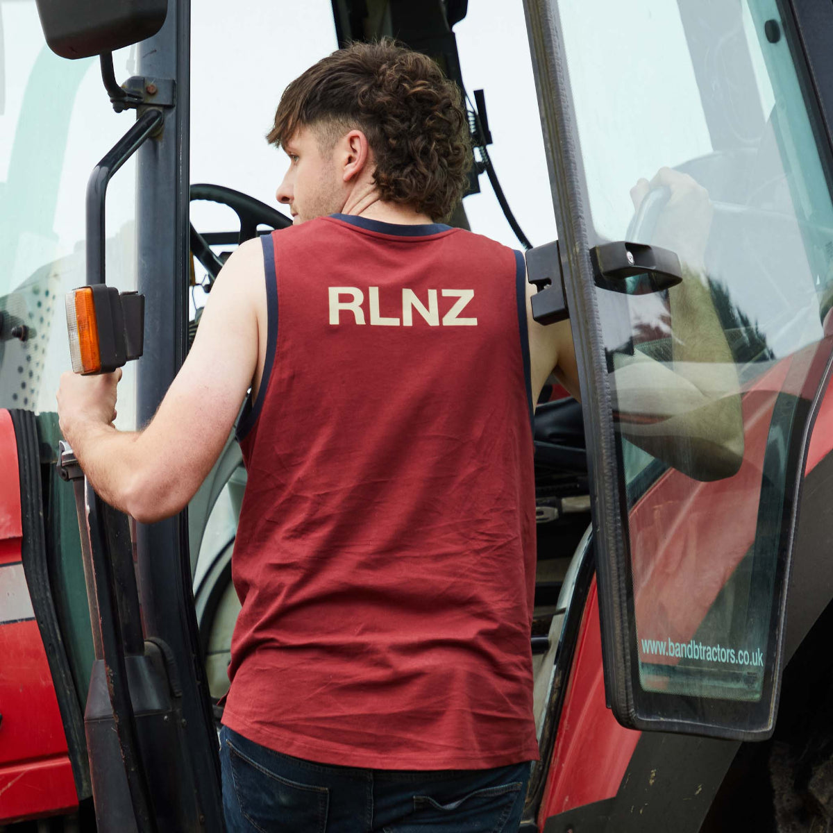 Person wearing a red 'RLNZ' tank top standing next to a large piece of machinery.
